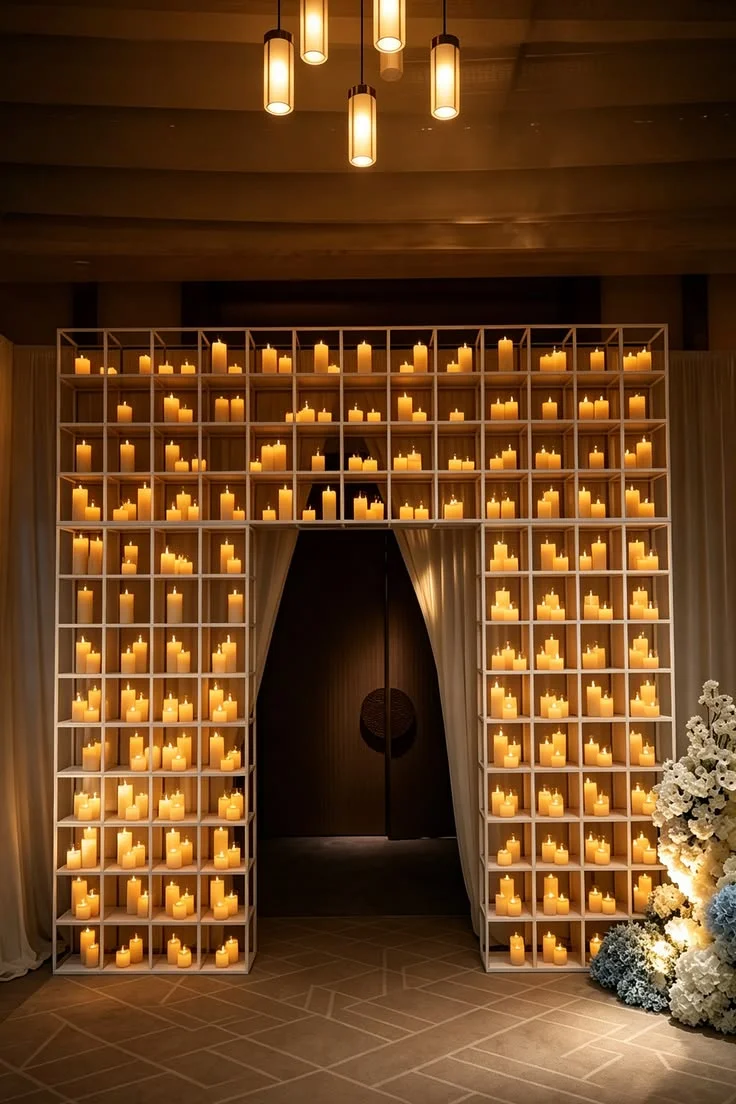 A wedding entrance framed by a white grid arch filled with warm flameless candles and flowers