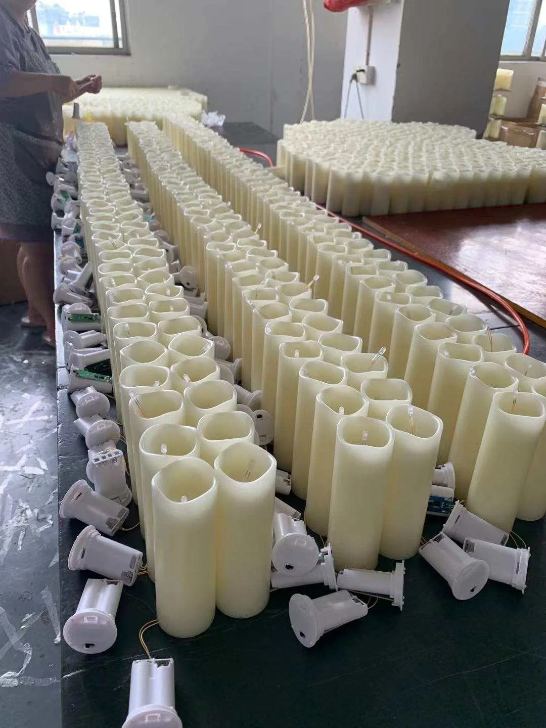 Cream coloured real wax LED candle bodies and electronic components arranged across a factory assembly table