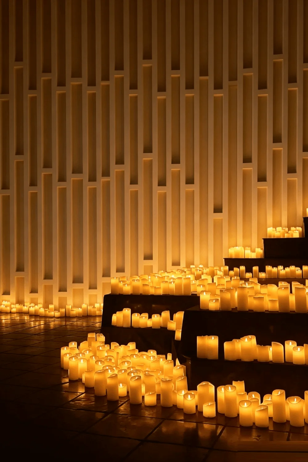 Hundreds of warm flickering flameless candles arranged on stepped platforms in a large event room