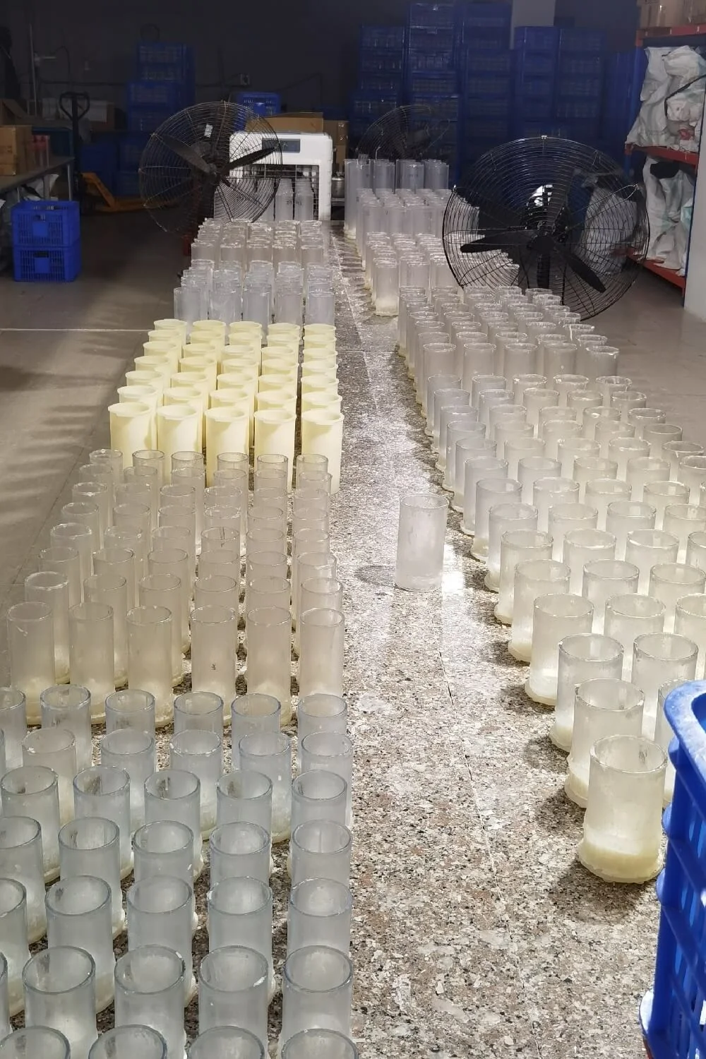 Rows of unfinished candle bodies and clear glass sleeves arranged on a factory worktable for wholesale production