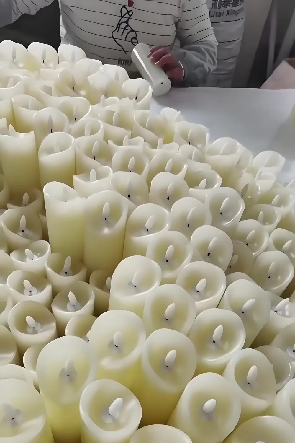 Close view of many white flameless pillar candle bodies with electronic wick assemblies being prepared on a worktable