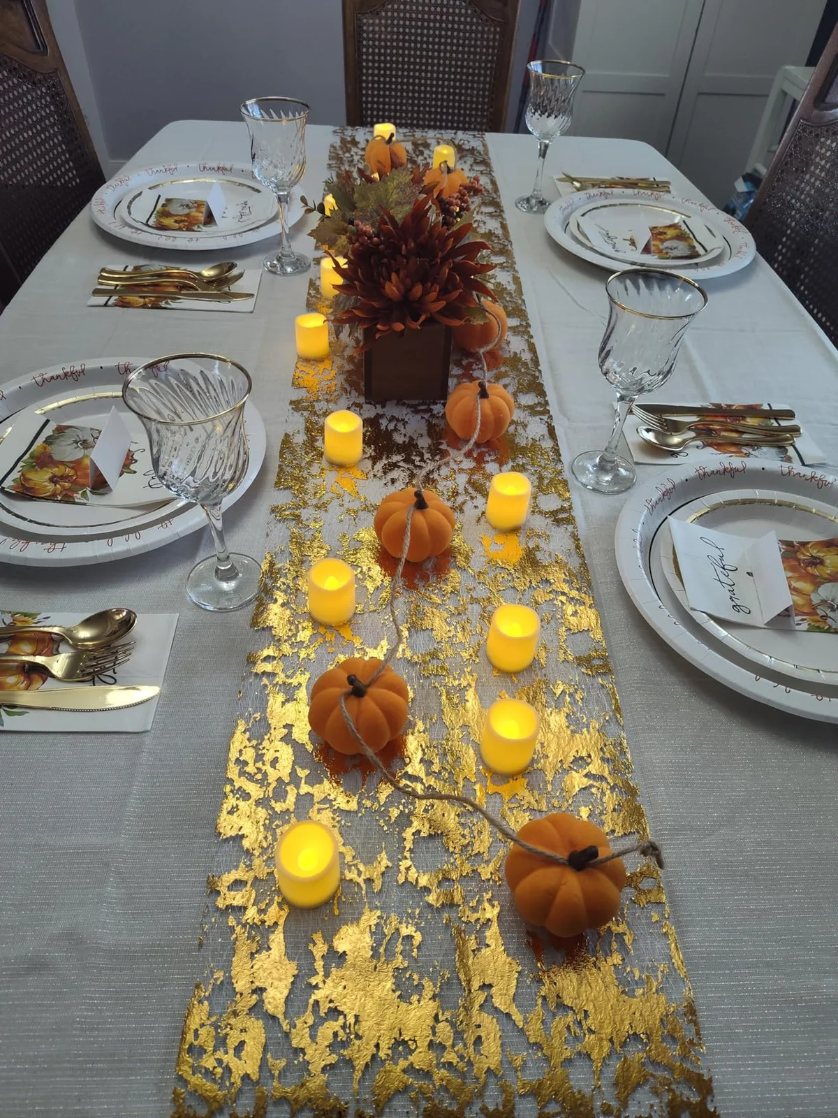 Small warm LED votive candles arranged along a decorated dining table with pumpkins and flowers