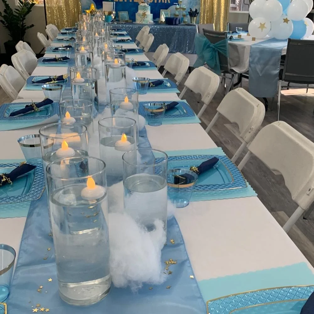 Flameless candles glowing inside clear glass cylinders along a blue and white decorated event table